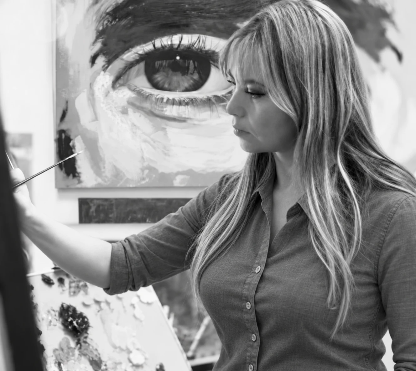 Patricia Vesga pintando al óleo en su estudio; al fondo, un ojo de gran formato de la serie Espejos del Alma.